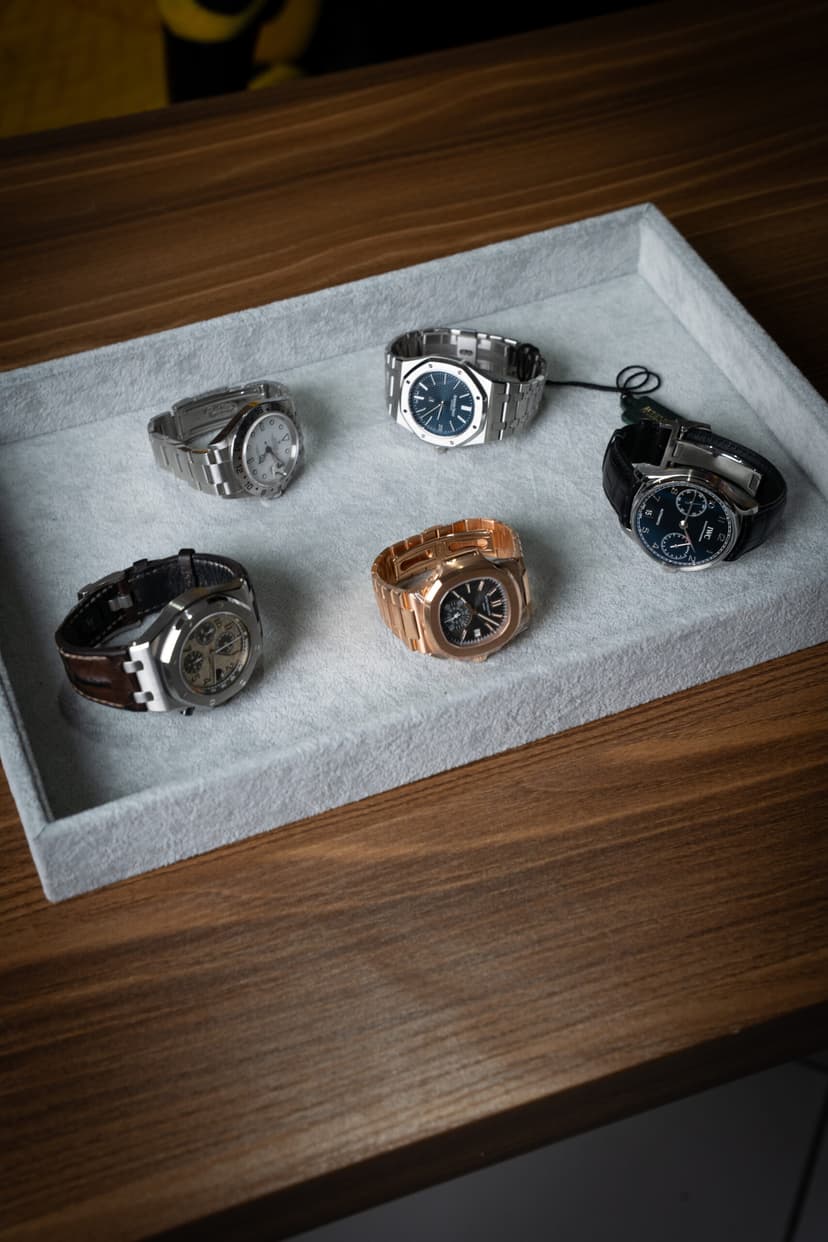 Cinq montres de luxe sur un plateau en feutre gris, posé sur une table en bois